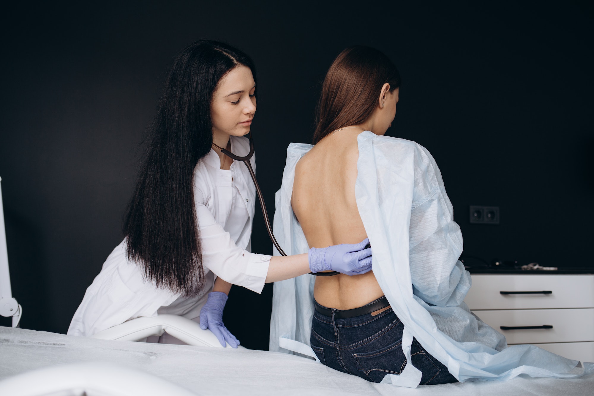 Doctor examining lungs of a female patient with stethoscope.