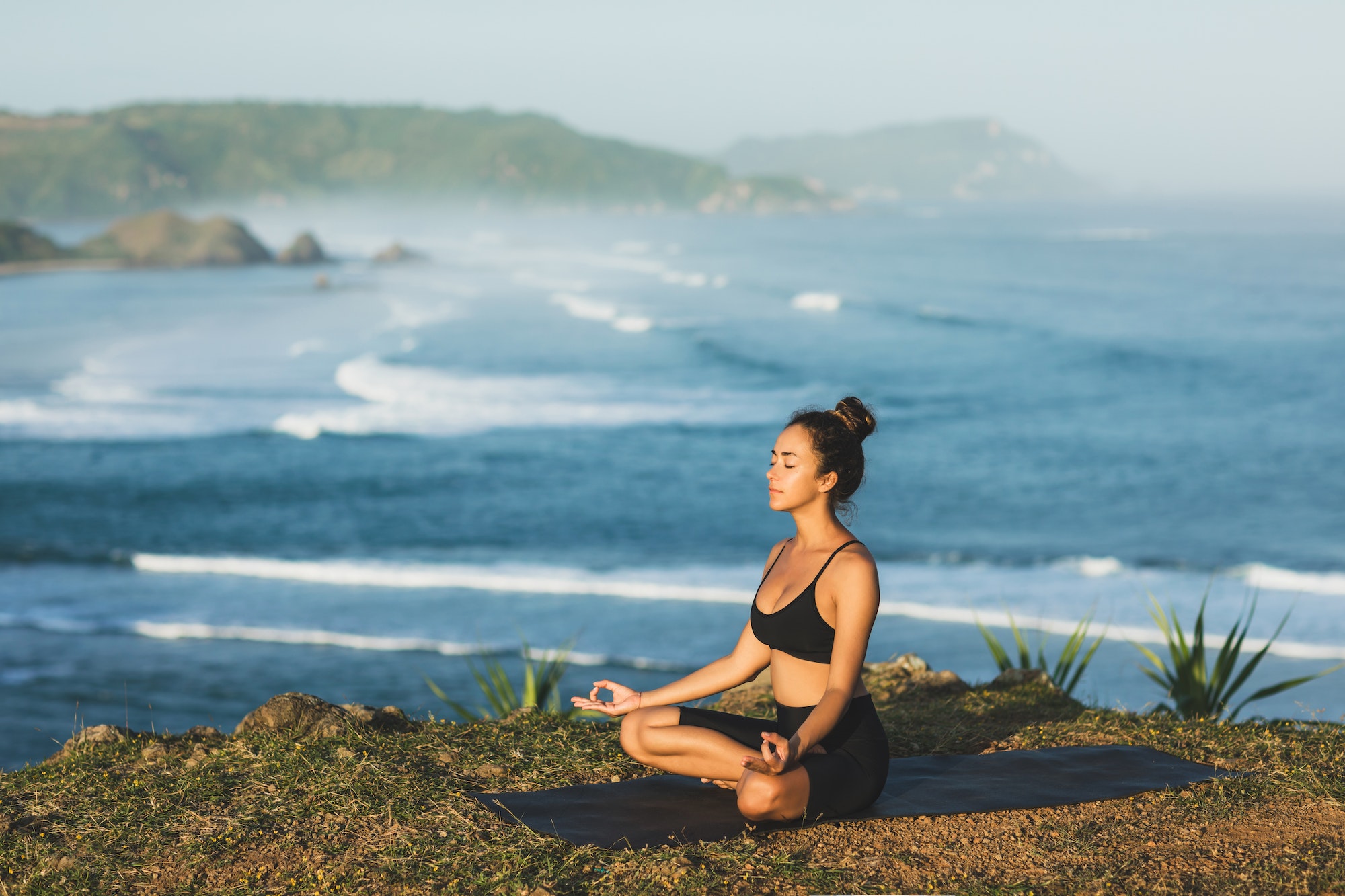 Woman practicing yoga and sit in lotus pose outdoor with amazing ocean view. Health and well-being